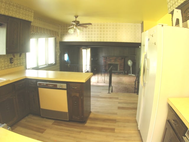 kitchen with a brick fireplace, white appliances, light hardwood / wood-style floors, ceiling fan, and kitchen peninsula