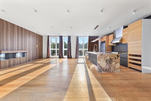 kitchen with light hardwood / wood-style flooring, wall chimney exhaust hood, a kitchen island with sink, built in refrigerator, and sink