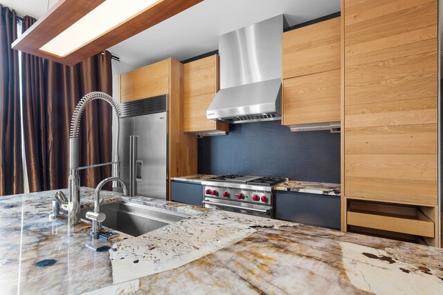 kitchen with sink, light stone countertops, light brown cabinetry, wall chimney range hood, and premium appliances