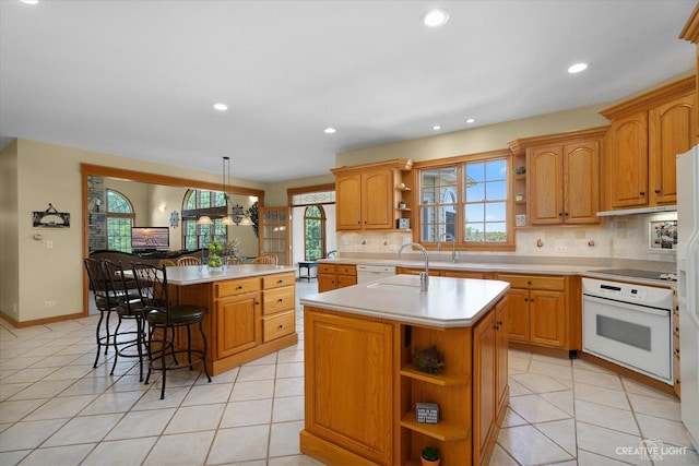 kitchen featuring kitchen peninsula, a kitchen island with sink, a breakfast bar, decorative light fixtures, and white appliances