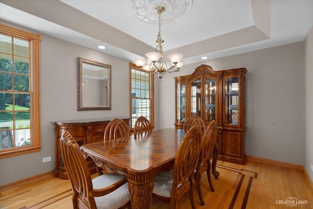 dining space with a tray ceiling, light hardwood / wood-style floors, and an inviting chandelier