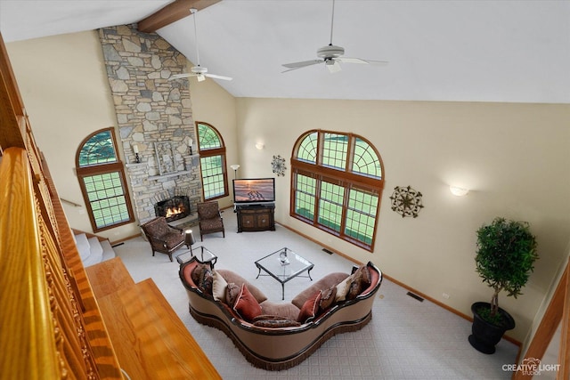 living room with a stone fireplace, ceiling fan, light carpet, high vaulted ceiling, and beam ceiling