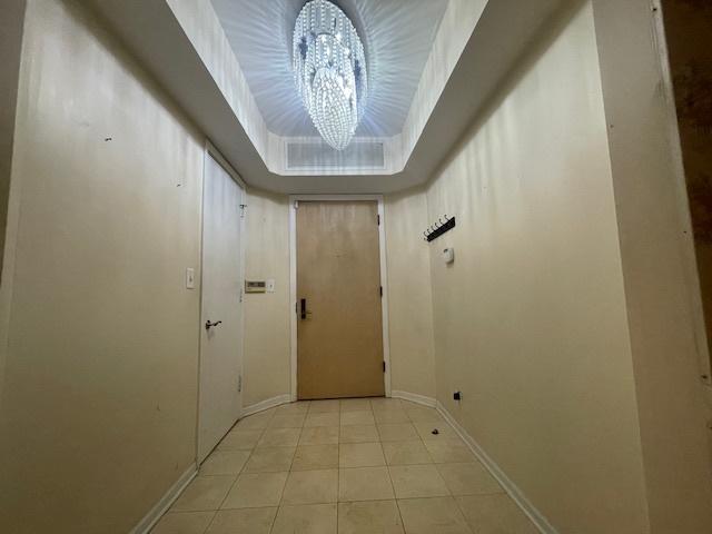 doorway to outside with a raised ceiling, a chandelier, and light tile patterned floors