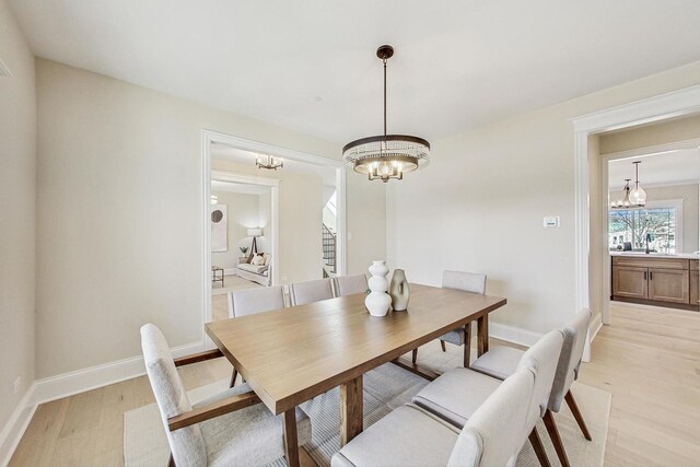 dining area featuring baseboards, light wood finished floors, and an inviting chandelier