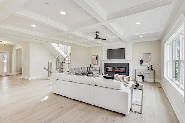 living area featuring stairs, coffered ceiling, a glass covered fireplace, and beam ceiling