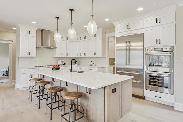 kitchen with wall chimney exhaust hood, stainless steel appliances, light wood-type flooring, white cabinetry, and a sink