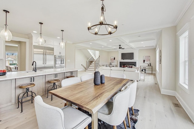 dining area featuring light wood-style flooring, coffered ceiling, beamed ceiling, and a lit fireplace