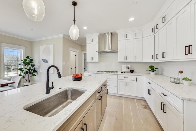 kitchen featuring light wood finished floors, crown molding, wall chimney range hood, gas stovetop, and a sink