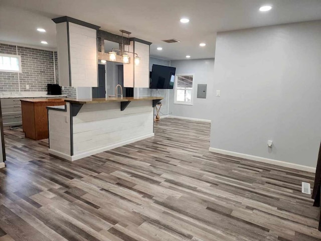 kitchen with decorative light fixtures, hardwood / wood-style floors, electric panel, kitchen peninsula, and a breakfast bar area