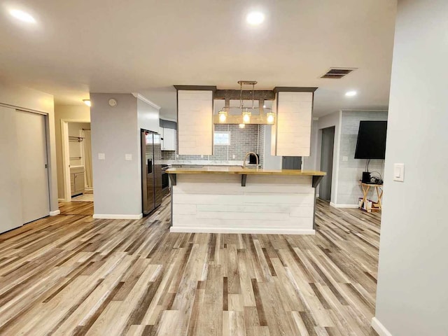 kitchen with light wood-type flooring, backsplash, pendant lighting, kitchen peninsula, and stainless steel fridge