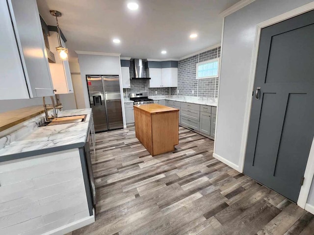 kitchen with appliances with stainless steel finishes, decorative backsplash, wall chimney range hood, wood-type flooring, and a center island