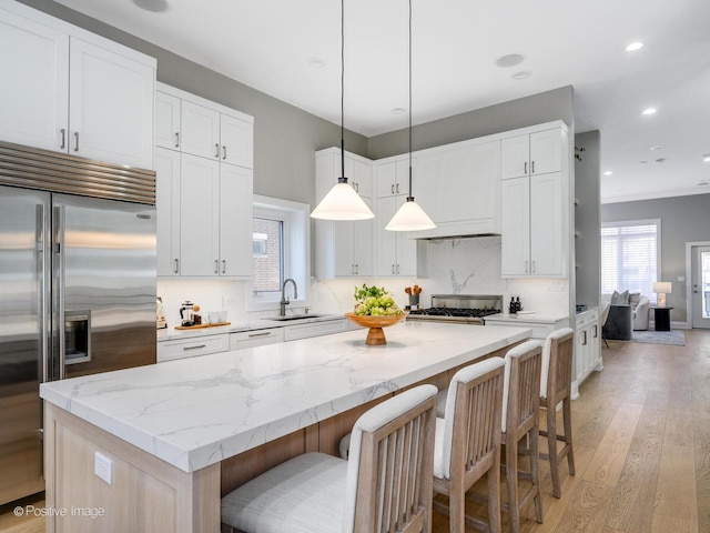 kitchen featuring white cabinetry, stainless steel built in fridge, a kitchen island, pendant lighting, and light hardwood / wood-style floors