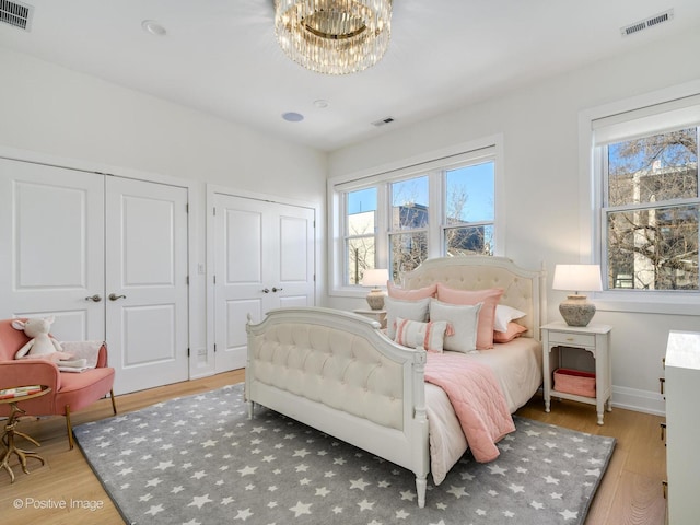 bedroom with two closets, hardwood / wood-style floors, and a notable chandelier