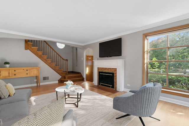 living room with a brick fireplace, ornamental molding, and light hardwood / wood-style flooring