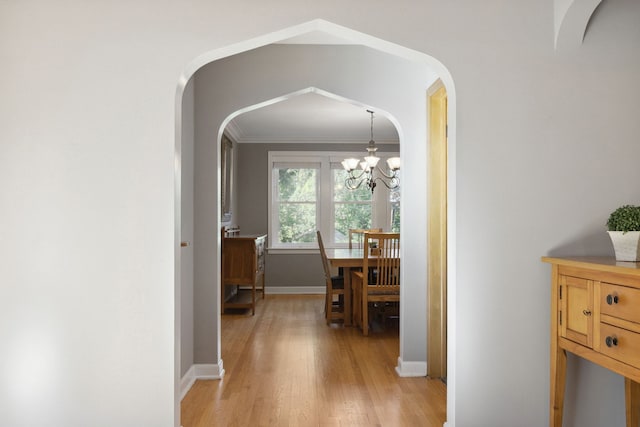 corridor with light wood-type flooring, ornamental molding, and an inviting chandelier