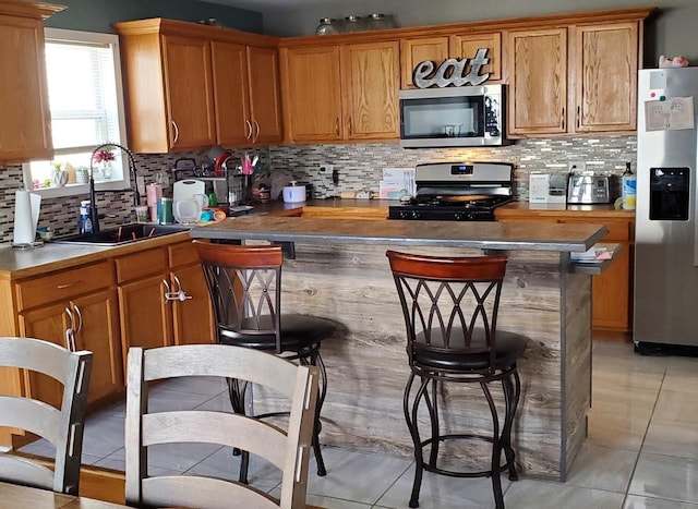 kitchen featuring light tile patterned floors, stainless steel appliances, tasteful backsplash, a sink, and a kitchen breakfast bar