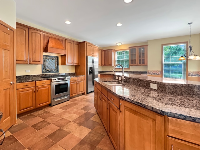 kitchen with hanging light fixtures, stainless steel appliances, sink, custom exhaust hood, and dark stone counters