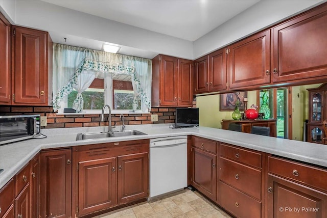 kitchen with white dishwasher, a toaster, a sink, light countertops, and tasteful backsplash