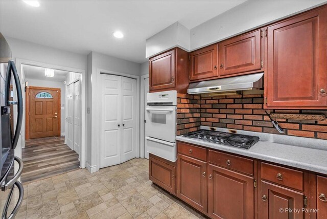 kitchen with light wood-type flooring, backsplash, black fridge, stainless steel gas cooktop, and double oven