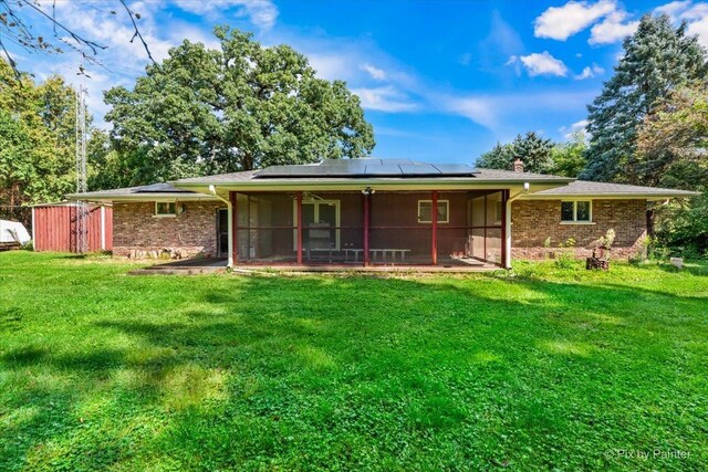 back of property with solar panels, a sunroom, and a lawn