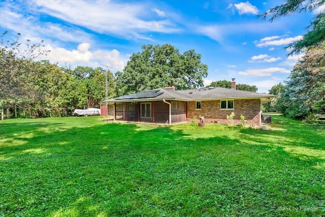 rear view of house with a sunroom, a yard, a chimney, and solar panels