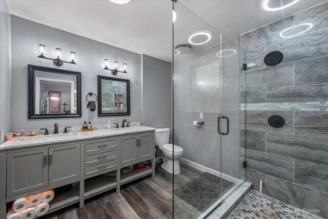 bathroom with wood-type flooring, toilet, vanity, and a shower with shower door