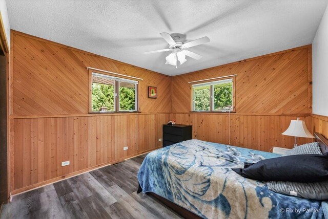 bedroom featuring hardwood / wood-style floors, a textured ceiling, wooden walls, and multiple windows