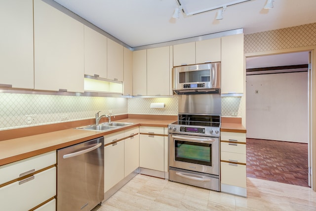 kitchen with sink, light hardwood / wood-style flooring, backsplash, track lighting, and stainless steel appliances