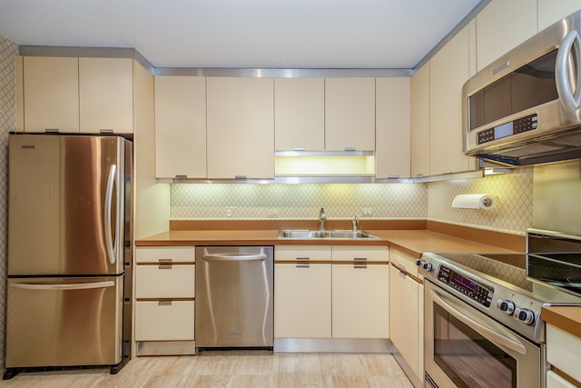 kitchen with stainless steel appliances, backsplash, light hardwood / wood-style floors, and sink