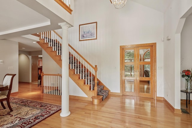 foyer with a towering ceiling, french doors, decorative columns, and hardwood / wood-style flooring