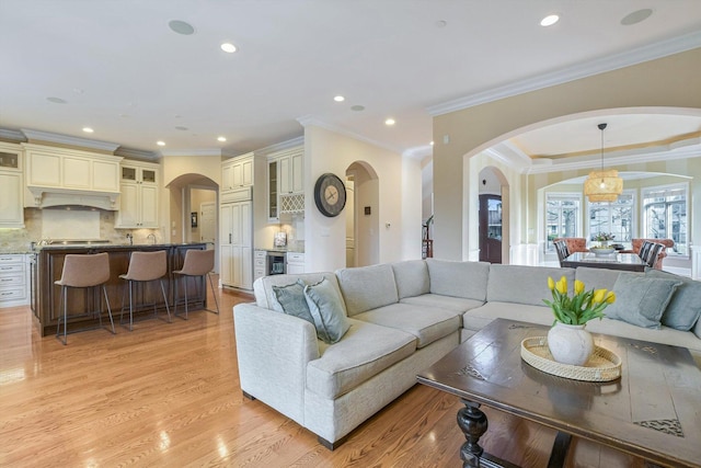 living room with arched walkways, recessed lighting, light wood-type flooring, and ornamental molding