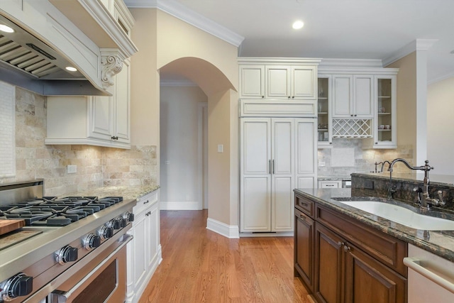 kitchen featuring a sink, arched walkways, appliances with stainless steel finishes, and dark stone countertops