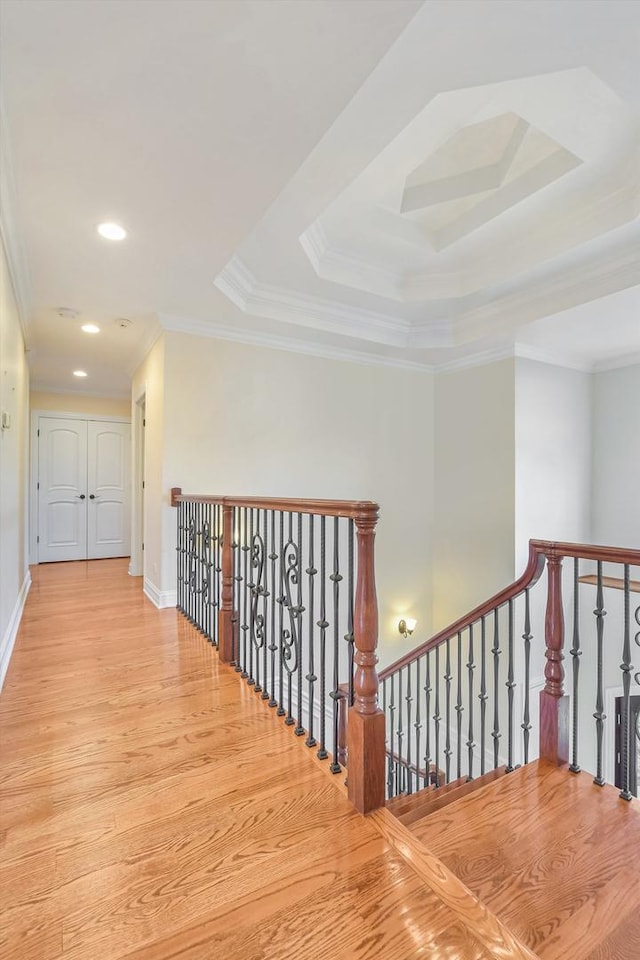 corridor with a tray ceiling, an upstairs landing, wood finished floors, and crown molding