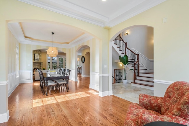 dining room featuring a raised ceiling, light wood-style floors, and arched walkways