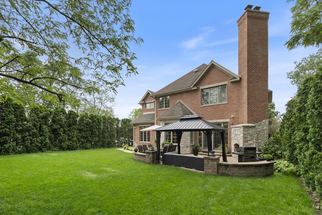 rear view of property featuring a gazebo, a yard, brick siding, a chimney, and a patio area