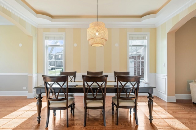 dining space featuring arched walkways, light wood-type flooring, and a tray ceiling