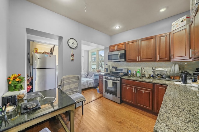 kitchen featuring backsplash, sink, dark stone countertops, light wood-type flooring, and appliances with stainless steel finishes