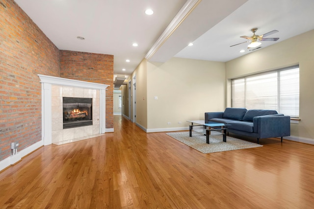 living room with brick wall, ceiling fan, light wood-type flooring, and a tile fireplace