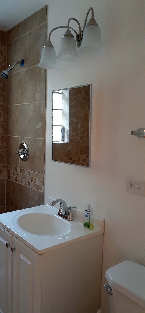 bathroom featuring a tile shower, vanity, and toilet