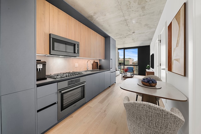 kitchen featuring sink, gray cabinetry, light hardwood / wood-style flooring, backsplash, and appliances with stainless steel finishes