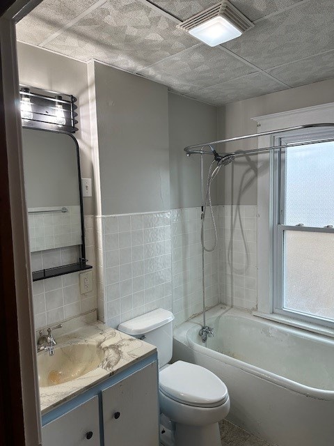 full bathroom with tiled shower / bath, toilet, vanity, and tile walls