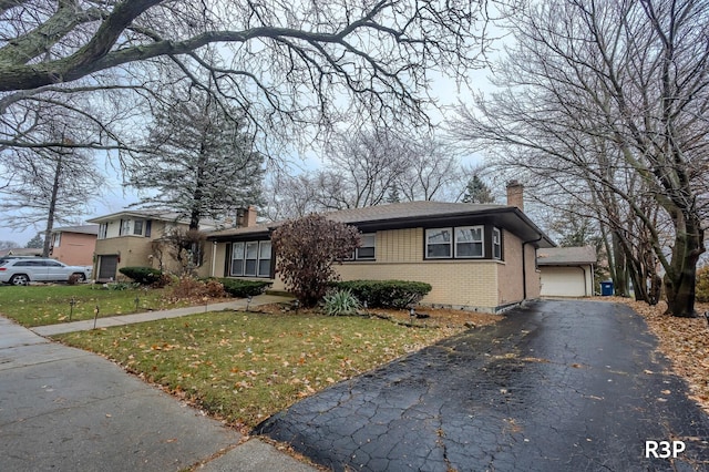 view of front of home featuring brick siding, an outdoor structure, driveway, a chimney, and a front yard