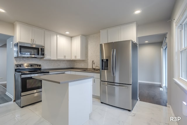 kitchen with appliances with stainless steel finishes, white cabinetry, tasteful backsplash, light wood-type flooring, and a center island