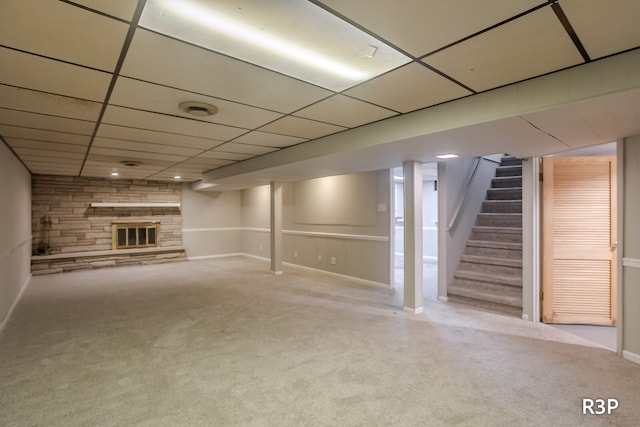 basement with light carpet, a paneled ceiling, and a stone fireplace