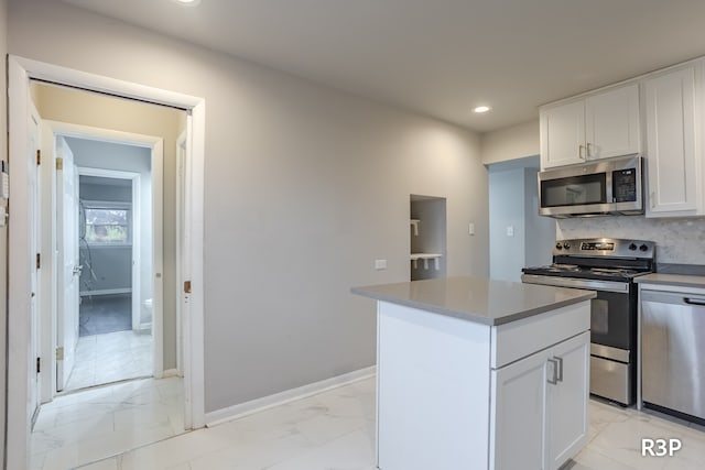 kitchen with appliances with stainless steel finishes, light tile patterned flooring, a kitchen island, and white cabinets