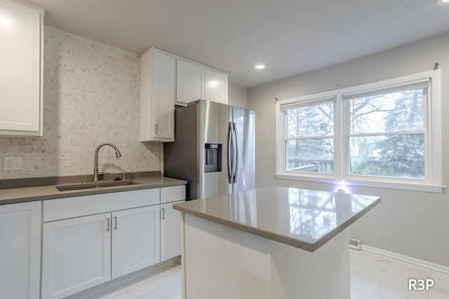 kitchen with stainless steel fridge, sink, a kitchen island, and white cabinets