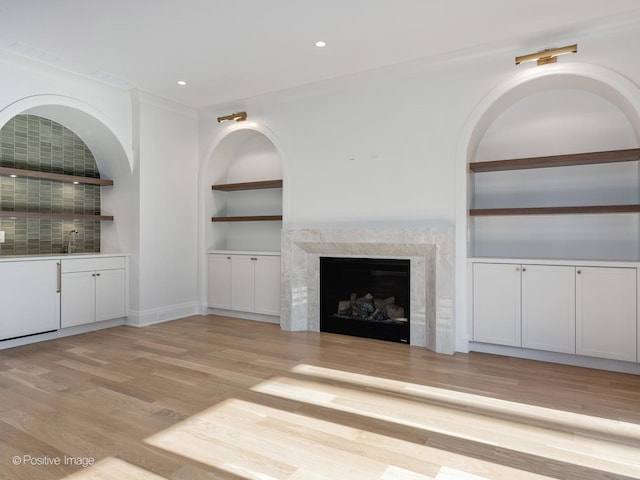 unfurnished living room featuring light wood-type flooring, sink, built in shelves, and a fireplace