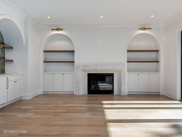 unfurnished living room featuring built in shelves, light wood-type flooring, and a high end fireplace