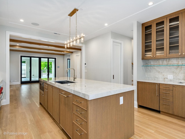 kitchen with backsplash, sink, beam ceiling, pendant lighting, and a center island with sink