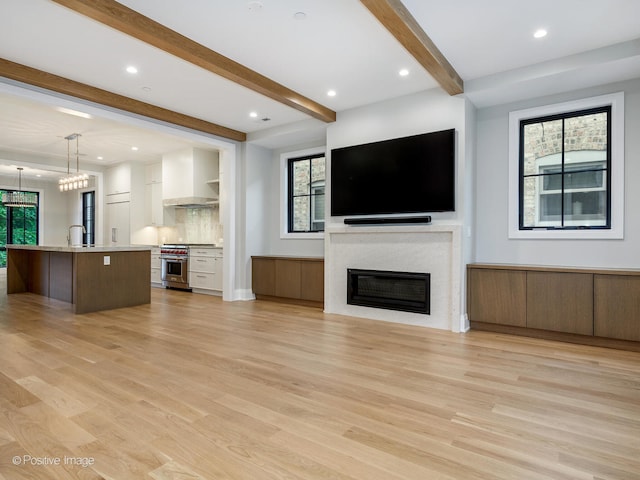 unfurnished living room with sink, beam ceiling, and light hardwood / wood-style floors